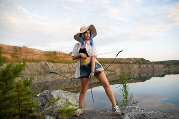 a beautiful girl in a blue wig and a straw hat with a bow and arrow in her hands.beautiful view of the lake and mountains.the concept of the game