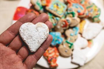 Hand holding a delicious handmade heart cookie and plate with more holiday cookies on a tea time table