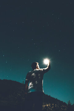 A young male looking at a star that he holds in hand at night