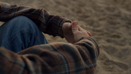 Unrecognizable man sitting on sandy beach alone. Closeup guy clasped hands