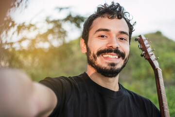 Young smiling Latin guitarist takes a selfie with his cell phone