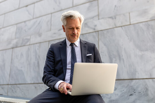 Professional Man Wearing A Suit Uses His Laptop While Sitting Outside