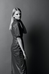 Fototapeta premium Fashion cool offer. Beautiful confident young woman looks over her shoulder at camera posing at studio background. Black and White concept. Art fashion photoshoot