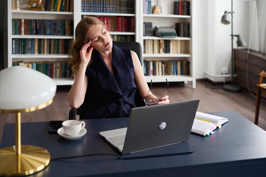 Overworked woman having migraine at table with laptop