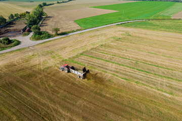 Top view of a tractor scattering manure from a trailer in the field. Work in the field near the road. Countryside. Natural fertilizer.