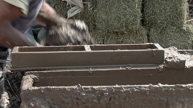 A Man Making Adobe Bricks (Mudbricks) as a Building Material, typically in the form of Sun-dried Bricks made from Earth and Organic Materials. Close Up.