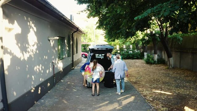 Done shot Group of people going on weekend citybreak while putting baggage inside vehicle. Casual family loading voyage luggage and trolleys inside car trunk while getting ready for summer holiday