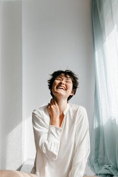 Cheerful young androgynous person laughing with closed eyes
