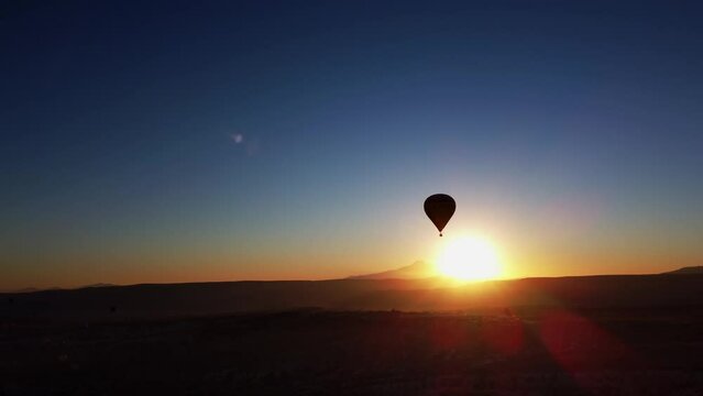 Aerial landscape of summer sunset over mountain range and rocky valley with hot air balloon in sky. Drone scenery of bright dusk over Cappadocia and a lonely flying vehicle with basket. Travel concept