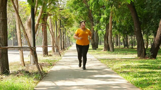 Fat Asian woman wearing yellow blouse Jogging in the morning In the park. Concept of weight loss Exercise for the good health of obese people. Copy space