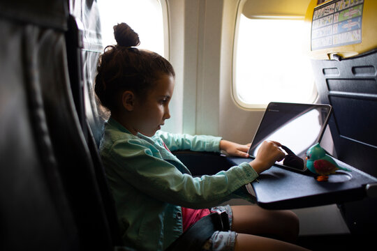 Kid sitting on window seat on airplane using tablet device.