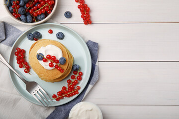 Tasty pancakes with natural yogurt, blueberries and red currants on white wooden table, flat lay. Space for text