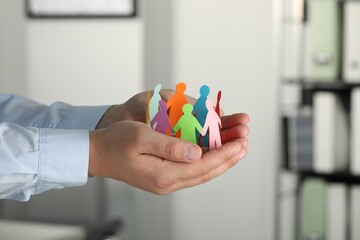 Man holding paper human figures in office, closeup. Diversity and Inclusion concept