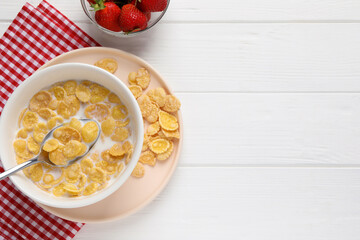Obraz na płótnie Canvas Bowl of tasty corn flakes and strawberries served on white wooden table, flat lay. Space for text