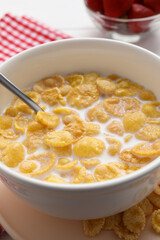 Bowl of tasty corn flakes served for breakfast on white wooden table, closeup