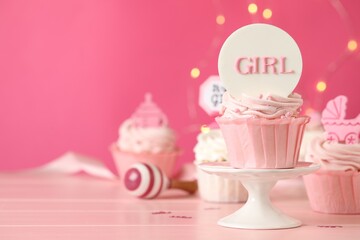 Beautifully decorated baby shower cupcakes with cream and girl toppers on pink wooden table. Space for text