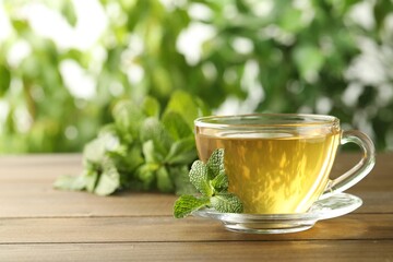 Glass cup of aromatic green tea with fresh mint on wooden table against blurred background. Space for text