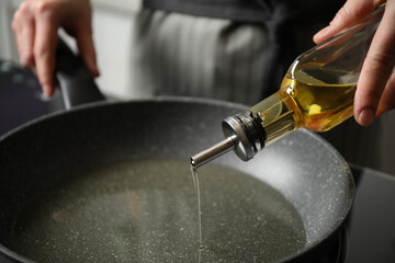 Woman pouring cooking oil from bottle into frying pan, closeup