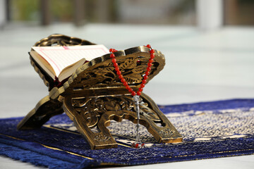 Rehal with open Quran and Misbaha on Muslim prayer rug indoors