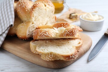 Cut freshly baked braided bread, knife and butter on white wooden table, closeup. Traditional Shabbat challah