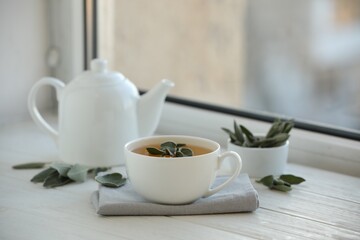 Sage tea and green leaves on white wooden windowsill