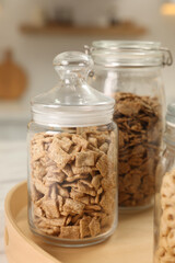 Glass containers with different breakfast cereals on white table in kitchen, closeup