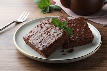 Fototapeta na wymiar Delicious chocolate brownies with fresh mint served on wooden table, closeup