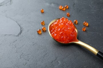 Spoon with delicious red caviar on black table, space for text