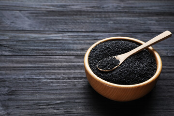 Bowl and spoon with black sesame seeds on wooden table, space for text