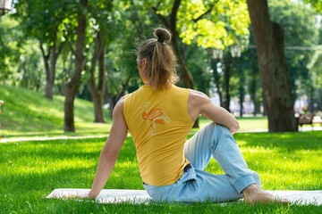 Young man practice yoga in the park. Yoga asanas in city park, sunny day. Concept of meditation,...