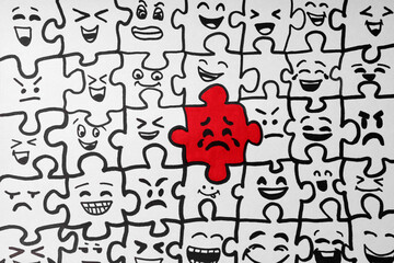 Drawing of white puzzle pieces and one red with different emotions, closeup. Bullying concept