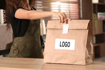 Woman holding paper bag with logo at counter in cafe, closeup
