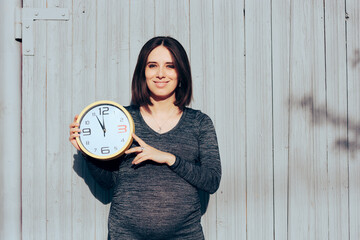 Beautiful Pregnant Woman Holding a Clock Showing Countdown. Mom counting the hours until the baby...