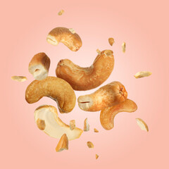 Tasty cashew nuts flying on pink background