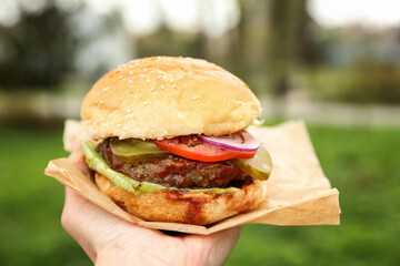 Little girl holding fresh delicious burger outdoors, closeup. Street food