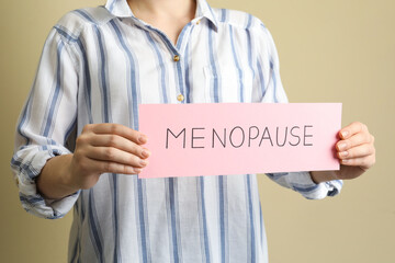 Woman holding card with word Menopause on beige background, closeup
