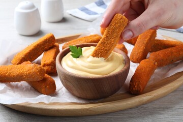 Woman dipping delicious chicken nuggets into cheese sauce at white wooden table, closeup