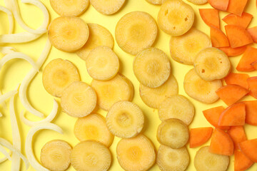 Pieces of raw color carrots on yellow background, flat lay