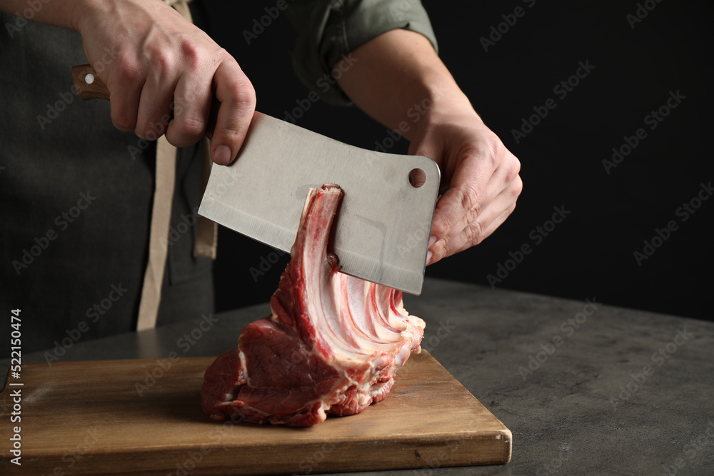 Wall mural Man cutting raw ribs at grey table, closeup