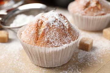 Tasty muffin powdered with sugar on table, closeup