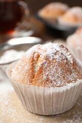 Tasty muffin powdered with sugar on table, closeup