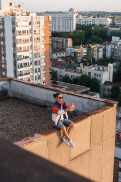 Man Sitting On The Edge Of A Rooftop And Using Phone