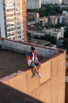 Man Sitting On The Edge Of A Rooftop And Looking At His Phone