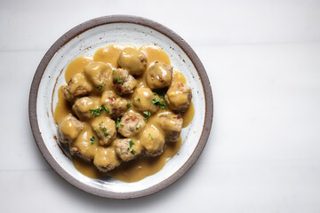 Swedish Meatball with brown mushroom sauce. Served on ceramic plate, on white table.