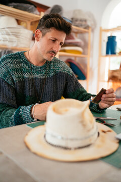 Talented craftsman decorating felt hat in atelier