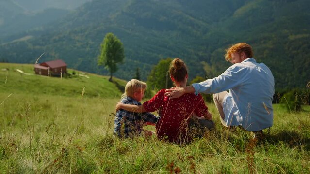 Relaxed family sitting grass mountain slope at summer. Parents hugging children.