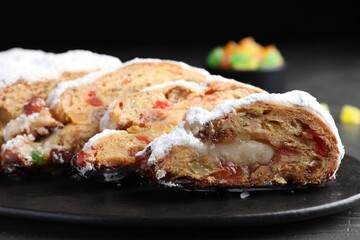 Traditional Christmas Stollen with icing sugar on black plate, closeup