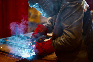 Fototapeta Skilled worker in protective mask welds metal part at plant obraz