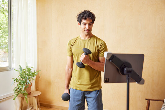 Fit man watching tablet and exercising with dumbbells