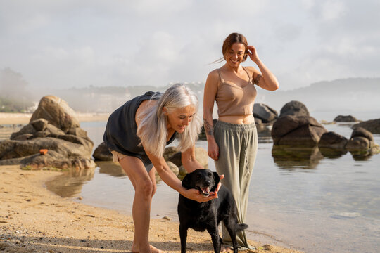 Portrait of happy mother and adult daughter at the beach with dog